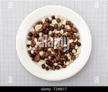 Caramelle in bianco e nero il cioccolato in un round piastra bianca sul tavolo. Candy, ciotola di uvetta, noci anf frutti ricoperti di cioccolato. Foto Stock