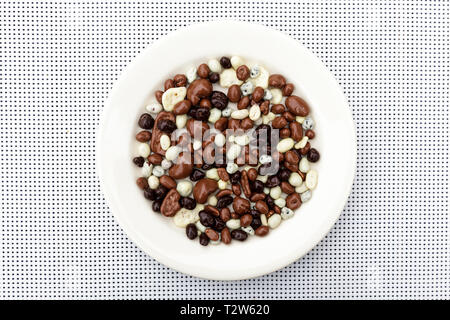 Caramelle in bianco e nero il cioccolato in un round piastra bianca sul tavolo. Candy, ciotola di uvetta, noci anf frutti ricoperti di cioccolato. Foto Stock