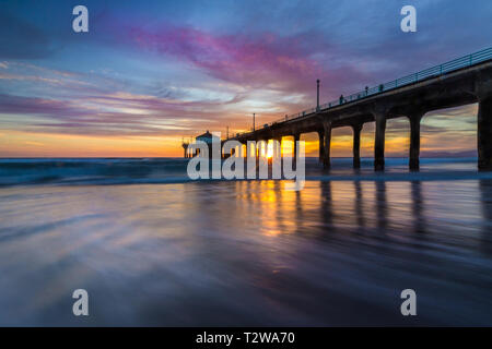 Lunga esposizione shot colorata del Cielo e nubi su Manhattan Beach Pier al tramonto con regolare lavaggio onde sulla spiaggia, Manhattan Beach, Californi Foto Stock