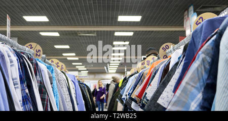 Eleganti camicie appesi in due righe su appendiabiti in negozio sono sfocate. Sullo sfondo sono sfocate acquirenti. Alla vigilia del Venerdì nero. Background fo Foto Stock