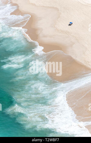 Fotografia aerea di acqua blu spiaggia con le onde che si propagano nella sabbia e una tenda sulla spiaggia. Foto Stock