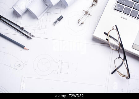 Computer portatile con diversi strumenti di disegno sui disegni. Stampe architettoniche e rulli da stampa e a strumenti di disegno sul piano di lavoro. Foto Stock