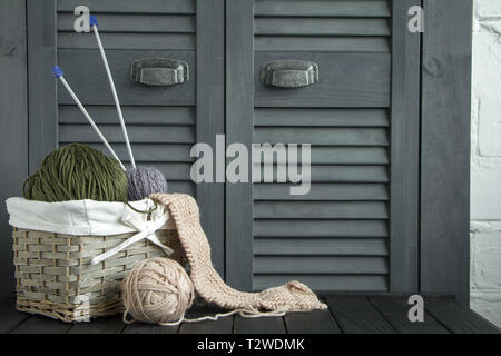 Tradizionali filati colorati per hobby maglia in una paglia eco cesto su uno sfondo grigio, biancheria da letto a maglia e la sfera del filato di colore beige. Foto Stock