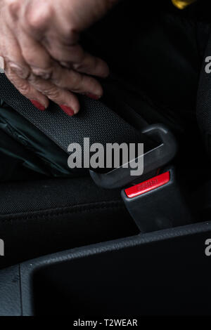 I vecchi senior donna allaccia la cintura di sicurezza in una macchina indossando verde e giacca gialla - non un salone in pelle Foto Stock