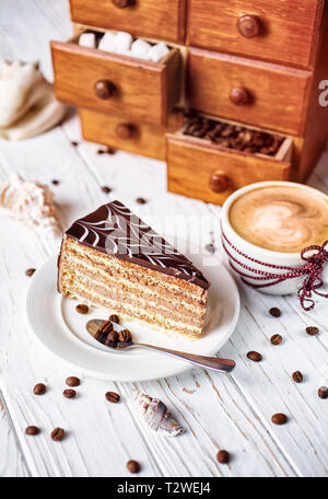 Torta al cioccolato con una tazza di cappuccino caldo sul tavolo con guscio. Foto Stock