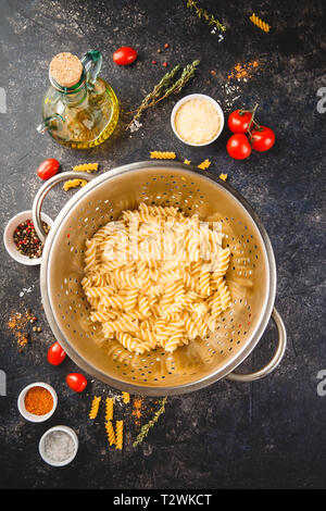 Fusilli in acciaio inox scolapasta e ingredienti su sfondo scuro. Vista superiore o flat-lay. Foto Stock