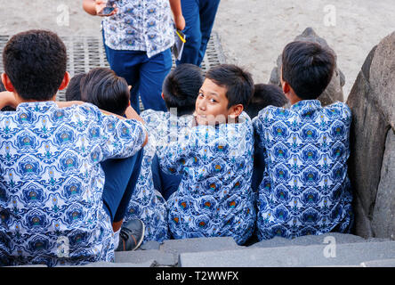 Uno dei giovani ragazzi della scuola seduta sulle scale a Vishnu santuari del tempio di Prambanan complesso è guardare indietro. Java, Indonesia Foto Stock