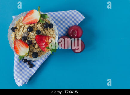 Ciotola con cereali per la prima colazione con fragole e bacche di colore rosso su sfondo blu. Vista dall'alto. Spazio per scrivere. Foto Stock