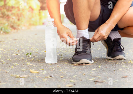 Immagine ritagliata di mani lacci delle scarpe di legatura su sneaker con una bottiglia di acqua Foto Stock