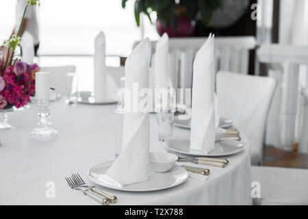 Closeup tovaglioli bianchi stand in piastre bianche sul tavolo serviti nel ristorante. Pulire piatti bianco formato su una tovaglia bianca. Foto Stock