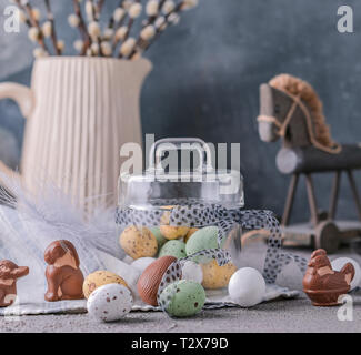 I rami di salici in un vaso su uno sfondo grigio e di uova di cioccolato per le vacanze di Pasqua. Un mazzetto di germogliare. Carta con fiori e dolci. Spazio di copia Foto Stock