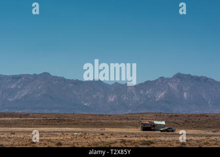 Un solitario shack e auto in mezzo alla vasta e secco paesaggio Namibiano, con il monte Brandberg in background Foto Stock
