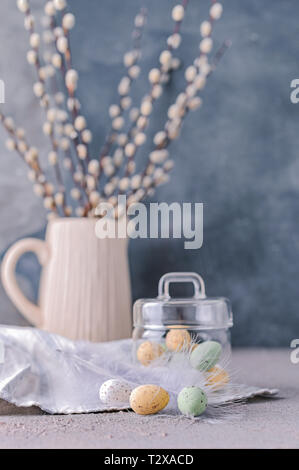 I rami di salici in un vaso su uno sfondo grigio e di uova di cioccolato per le vacanze di Pasqua. Un mazzetto di germogliare. Carta con fiori e dolci. Spazio di copia Foto Stock