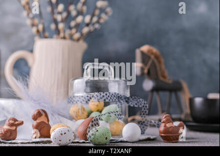 I rami di salici in un vaso su uno sfondo grigio e di uova di cioccolato per le vacanze di Pasqua. Un mazzetto di germogliare. Carta con fiori e dolci. Spazio di copia Foto Stock