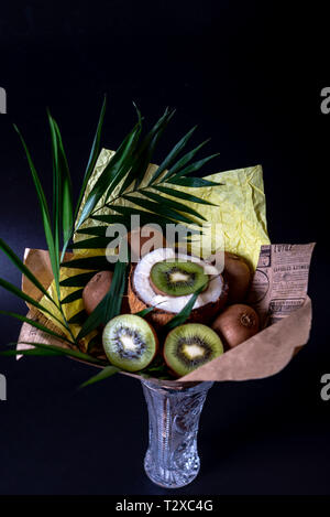 Unico bouquet di festa della noce di cocco, kiwi e palm ramoscelli su uno sfondo nero. Bouquet vegetale. Frutta e verdura di un sano concetto. Foto Stock