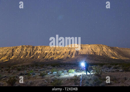 Un uomo escursioni attraverso il deserto sotto le stelle nella roccia rossa, il Nevada. Foto Stock