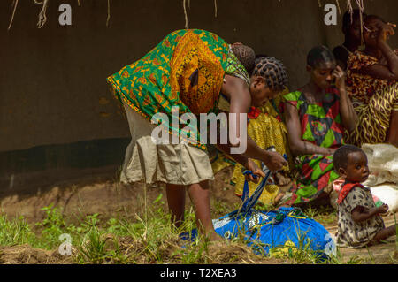 La donna che porta il bambino sulla schiena lega il suo tessuto di cotone tenendo il granturco aiuti nel villaggio Malawi Foto Stock