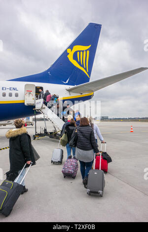 I passeggeri di salire a bordo di un volo su un aereo Ryanair tirando lungo il bagaglio carrellato come bagaglio a mano per andare negli armadietti soprastanti Foto Stock