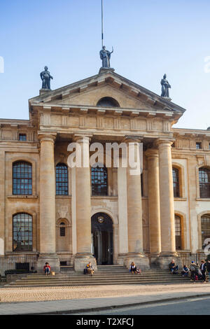 Turisti e studenti sedersi sui passi dei primi anni del XVIII secolo Clarendon Building in Broad Street, Oxford Foto Stock