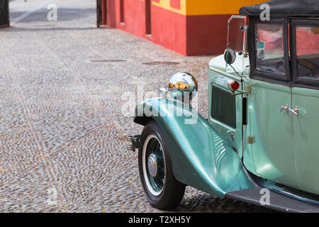 Parafango, la ruota e il faro anteriore di una annata 1932 auto parcheggiate in Fortaleza de Sao Tiago a Funchal. Verde auto, nichelato lucido, proiettore vecchio acciottolato Foto Stock