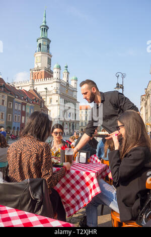 Persone uomini e donne seduti fuori a mangiare e a bere al caffè nel caldo sole primaverile in piazza della città vecchia nella città polacca di Poznan in Polonia Foto Stock