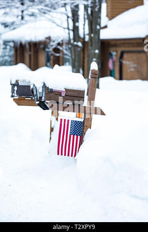 Coperta di neve di cassette postali con bandiera attaccata e una bandiera sulla casa. Foto Stock