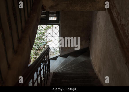 Dark stair discesa in una vecchia casa con luce naturale proveniente da una finestra sbarrata. Il Palazzo o Villa Bodega, Phnom Penh Cambogia. Foto Stock