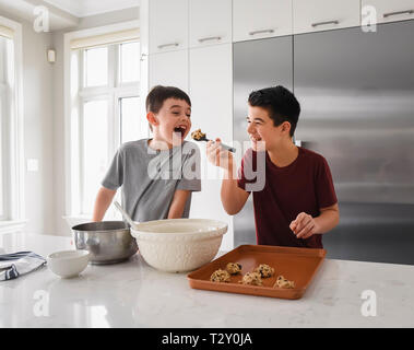 I vecchi boy alimentazione di pasta biscotto al giovane ragazzo in cucina moderna Foto Stock