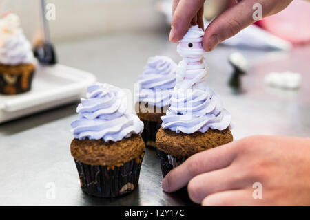 Lo Chef mano viene aggiunta una mummia morbido su un mirtillo crema di burro cupcake Foto Stock