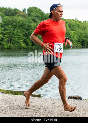 Babilonia, New York, Stati Uniti d'America - 12 August 2018: un runner è in esecuzione un 10.000 metri di gara con nessuno scarpe on, off road nelle prove passando un lago durante il Di Foto Stock