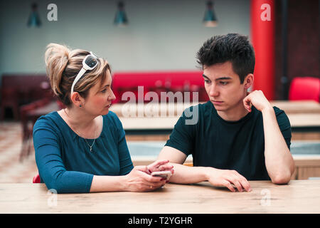 Donna e uomo giovane parlare insieme e utilizzando i telefoni cellulari seduti a un tavolo in cafe Foto Stock