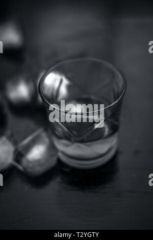 Close up di Scotch whisky di grano o di scotch in un vetro trasparente con cubetti di ghiaccio sul colore nero la superficie di legno. Foto Stock