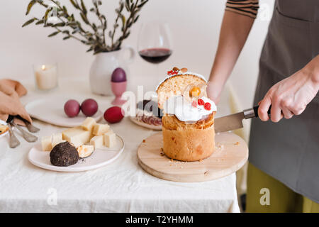 Tagliare la torta di Pasqua in mano womans. La pasqua ortodossa tradizionale pane dolce, kulich. Vacanze di Pasqua a colazione. Taglio femminile torta di Pasqua. Foto Stock