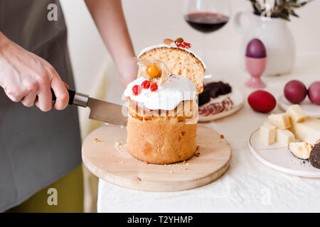 Tagliare la torta di Pasqua in mano womans. La pasqua ortodossa tradizionale pane dolce, kulich. Vacanze di Pasqua a colazione. Taglio femminile torta di Pasqua. Foto Stock