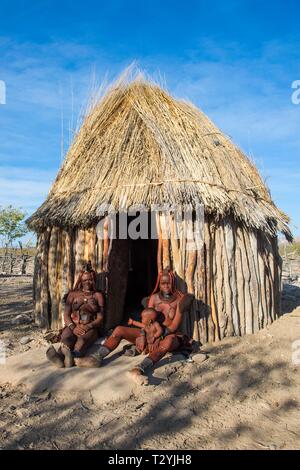 Le donne himba davanti alla loro capanna in legno, Kaokoland, Namibia Foto Stock