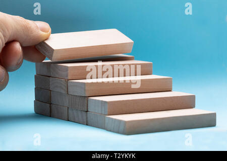 Mano d'uomo disponendo il blocco di legno come stacking passo su sfondo blu Foto Stock