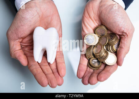 Una vista in alzata di mano d'uomo Azienda Dente Bianco e monete d'oro su scrivania Foto Stock