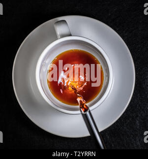 Il caffè e la crema versando in una tazza bianca su un piattino bianco con sfondo nero Foto Stock