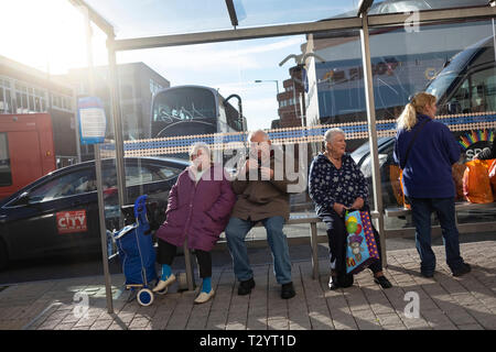 Coppia di anziani e gli altri a una fermata degli autobus in una luminosa giornata di sole in inverno a Sheffield Foto Stock