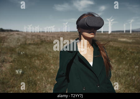 Donna che indossa le cuffie VR al campo accanto alle turbine eoliche Foto Stock