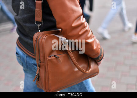 Uomo con borsa in pelle sulla sua spalla. Il ragazzo sta camminando per la strada Foto Stock