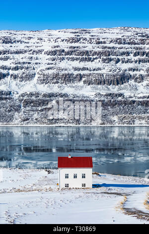 Casa con il tetto rosso nel drammatico paesaggio invernale lungo il fiordo Ísafjarðardjúp nei pressi di Ísafjörður nella regione Westfjords, Islanda [alcuna proprietà di rilascio; av Foto Stock