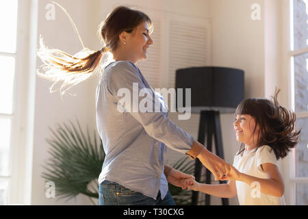 Madre tenendo le mani con la figlia ballando e saltando a casa Foto Stock