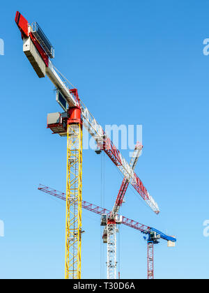 Basso angolo vista di tre grandi gru a torre su un sito di costruzione contro il cielo blu. Foto Stock