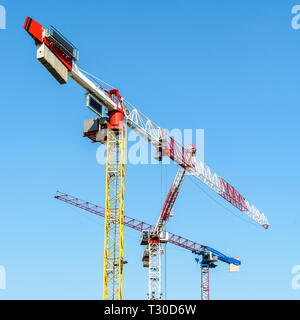 Basso angolo vista di tre grandi gru a torre su un sito di costruzione contro il cielo blu. Foto Stock