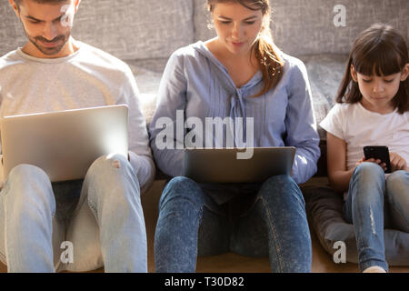 Famiglia con bambino seduto sul pavimento assorbita in dispositivi digitali Foto Stock