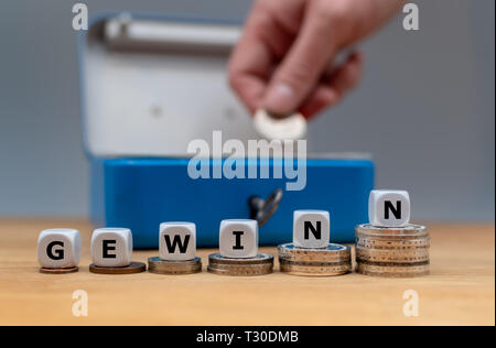 Simbolo di aumentare i profitti. Dadi formano la parola tedesca "Gewinn' ('utile" in inglese). Dadi posti su pile di monete. Una scatola di denaro è in backgrou Foto Stock