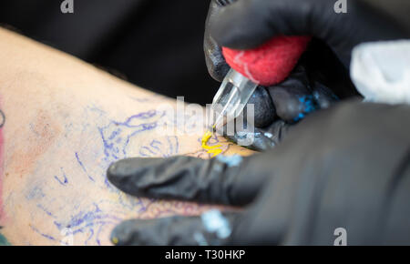 Primo piano di un tatuaggio nella realizzazione (ago per tatuaggio che applica inchiostro giallo sulla pelle) Foto Stock