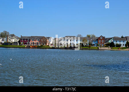 Vista di case attraverso il lago a Watermead, Aylesbury, Buckinghamshire, UK Foto Stock