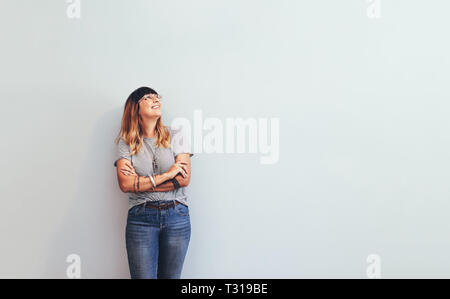 Donna sorridente in jeans e maglietta in piedi contro un muro che guarda lontano. Imprenditore in piedi con le mani giunte. Foto Stock